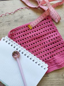 A pink crochet sample with a tape measure and notebook, perfect for creative DIY projects.