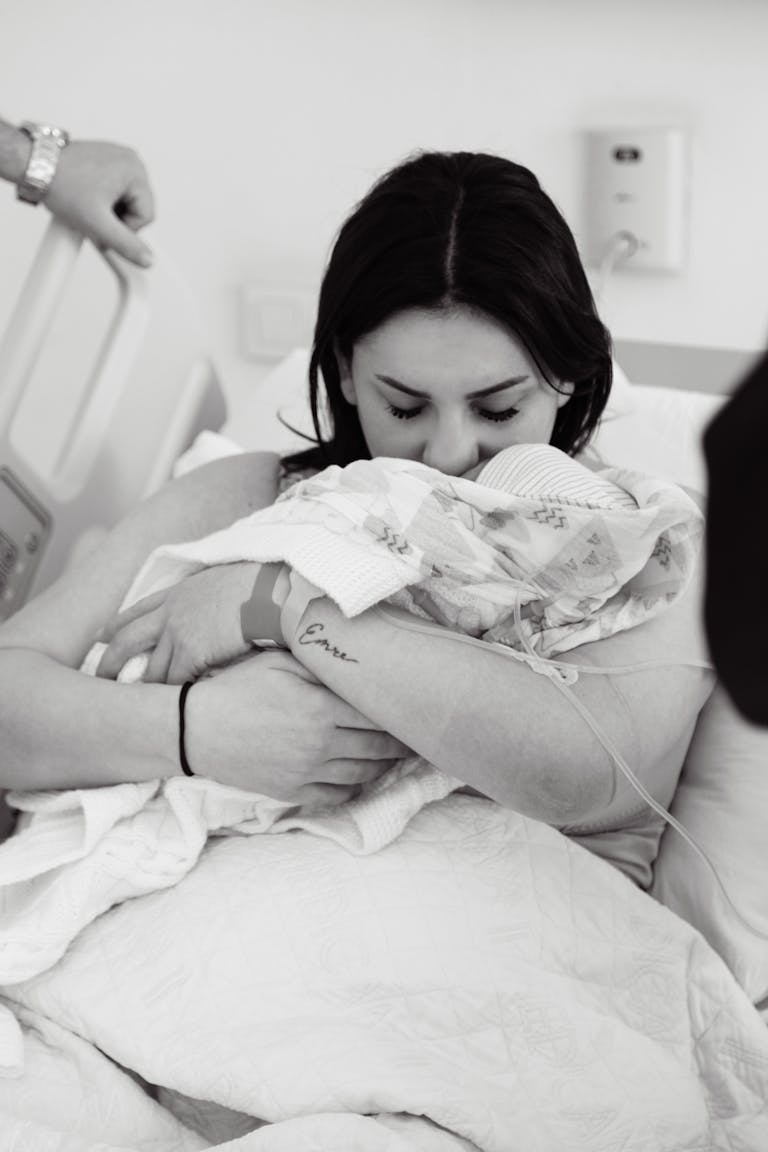 A touching black and white photo of a mother lovingly holding her newborn in a hospital bed.